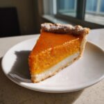 A close-up shot of a slice of easy pumpkin pie showing a bright orange pumpkin layer over a white base layer, served on a white plate.