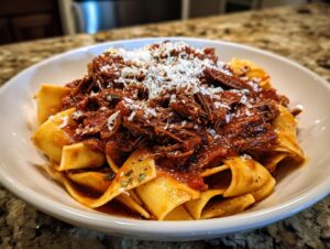 Close-up of a white bowl filled with wide pappardelle pasta topped generously with rich beef ragu and grated Parmesan cheese.