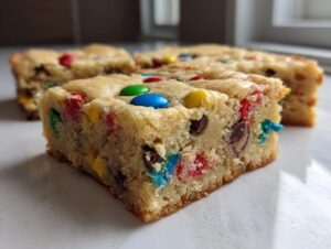 A thick, chewy slice of Christmas cookie bars studded with colorful M&M-style candies and chocolate chips.