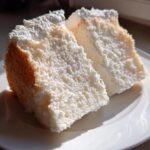Two fluffy, white slices of angel food cake showing their airy texture, served on a white plate.