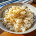 Close-up of a white bowl filled with fluffy white butter rice topped with golden garlic bits and herbs.