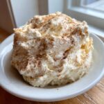 A fluffy, whipped mound of homemade cinnamon butter sprinkled generously with ground cinnamon on a white saucer.