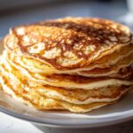 Close-up of a tall stack of fluffy oatmeal pancakes with golden-brown, lacy edges.
