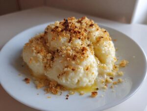 Close-up of fluffy potato dumplings topped generously with golden brown buttered breadcrumbs.