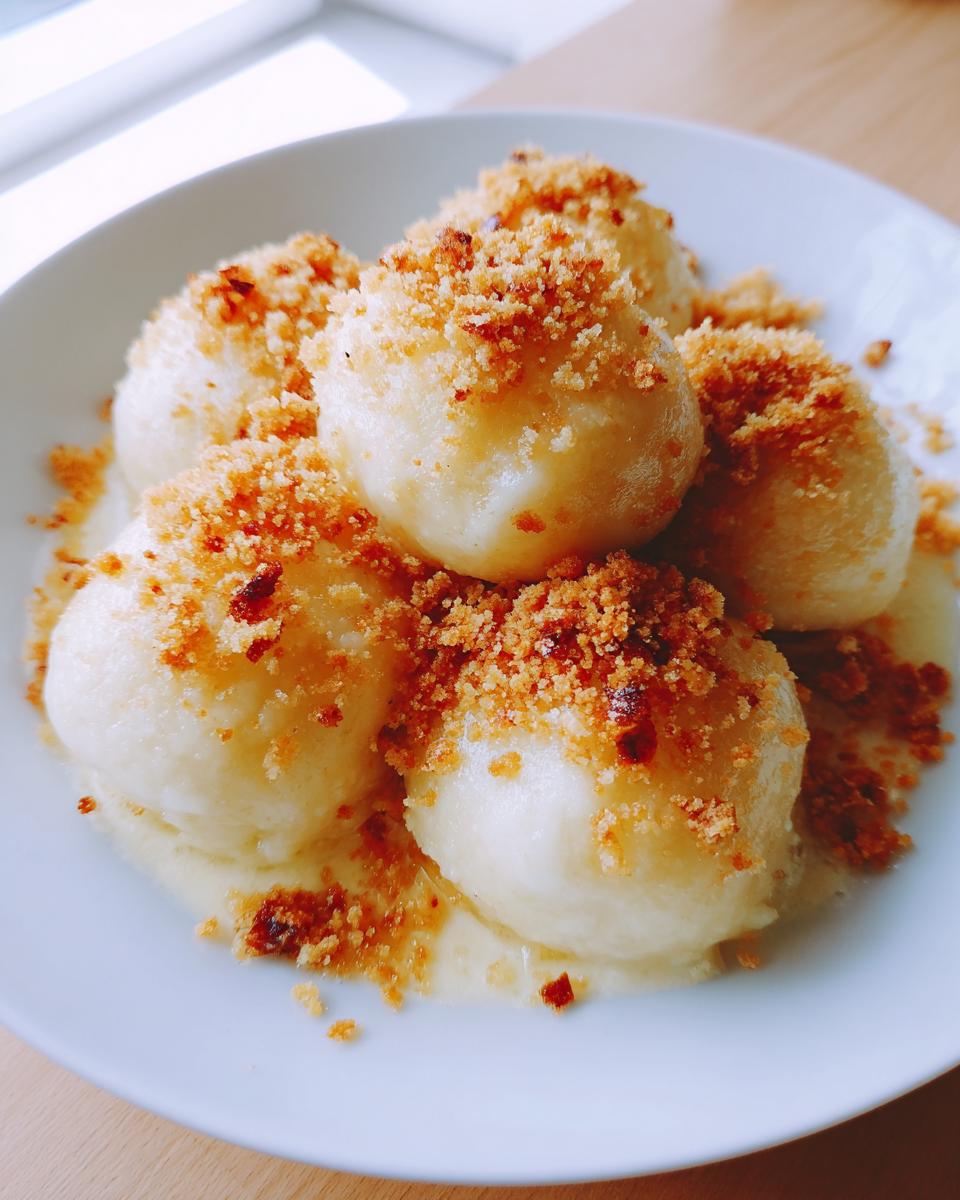 Close-up of fluffy potato dumplings served on a white plate, generously topped with toasted breadcrumbs.