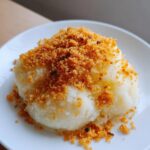 Close-up of fluffy potato dumplings served on a white plate and generously topped with golden brown breadcrumbs.