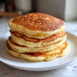 A tall stack of four fluffy sourdough pancakes with golden brown tops on a white plate.