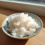 A close-up of perfectly cooked, fluffy sushi rice piled high in a small, light green ceramic bowl.