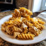 A fork lifting a bite of cheesy chicken pasta made with rotini noodles and melted cheddar cheese.