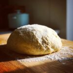 A perfectly rounded ball of freshly kneaded pizza dough resting on a floured wooden surface.