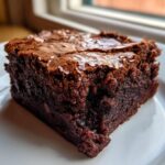 Close-up of a rich, fudgy square of brownies showing a shiny, crackled top crust.