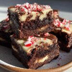 Close-up of stacked, fudgy candy cane brownies topped with white chocolate and crushed peppermint candy.