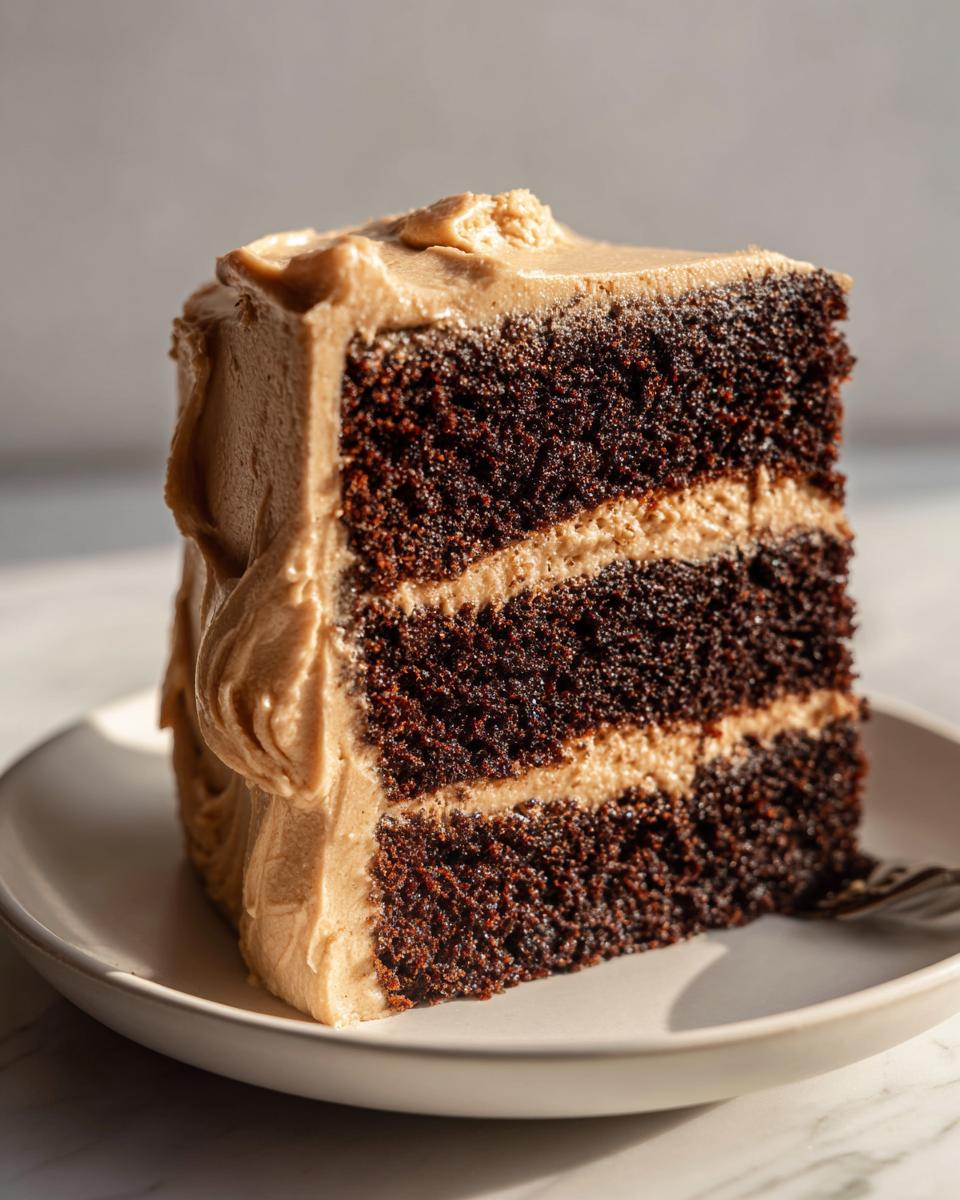 A tall slice of dark chocolate gingerbread latte cake with layers of light brown coffee frosting.