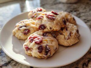 A stack of freshly baked cranberry orange cookies drizzled with white glaze, sitting on a white plate.