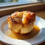 A single, golden brown apple dumpling drenched in sweet caramel sauce, served on a white plate.