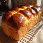 A freshly baked, glossy loaf of japanese milk bread cooling on a wire rack.