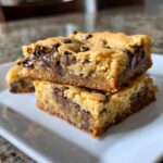 Two rich, thick cake mix cookie bars stacked on a white plate, featuring melted chocolate chips.