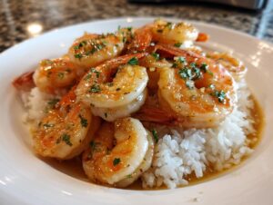 Close-up of succulent hawaiian garlic shrimp glazed in sauce and sprinkled with parsley, served over a bed of white rice.