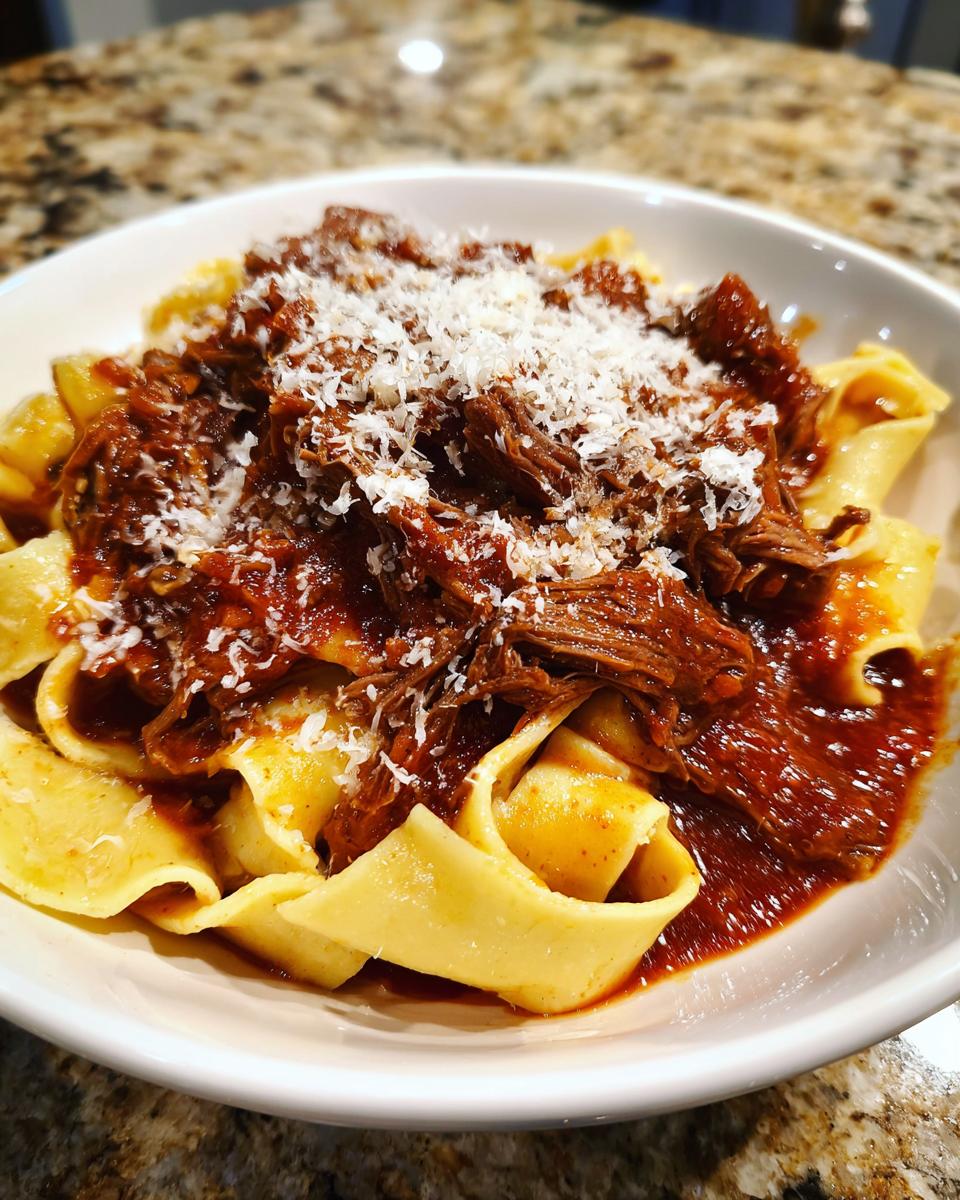 A close-up of a bowl filled with wide pappardelle pasta topped generously with rich beef ragu and grated Parmesan cheese.