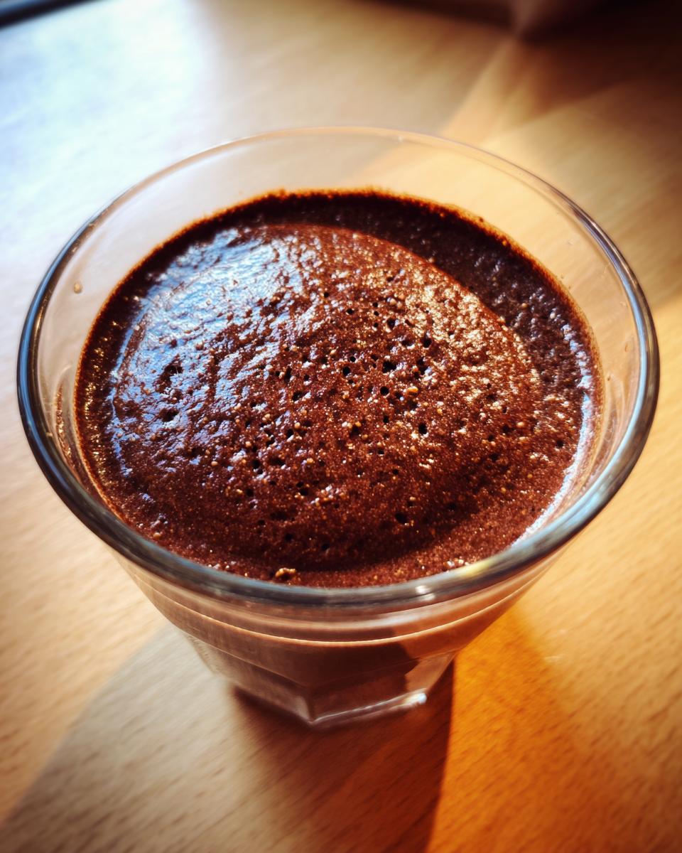 Close-up of rich, dark homemade chocolate pudding with a slightly foamy top in a clear glass.