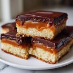 Close-up of stacked homemade twix bars showing shortbread, gooey caramel, and chocolate topping.