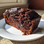 A rich, dark slice of hot fudge brownie bread topped with melted chocolate sauce on a white plate.