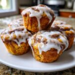 A stack of freshly baked cinnamon roll muffins topped with thick white icing, ready to eat.