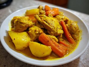 A close-up of vibrant Jamaican curry chicken served with chunks of potato and bright orange carrots.