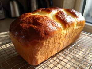 A golden brown, glossy loaf of freshly baked japanese milk bread cooling on a wire rack.