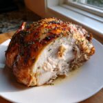 A cross-section of a juicy, herb-crusted turkey breast showing moist white meat on a white plate.