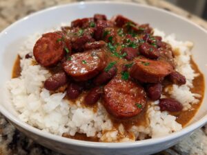A close-up of creamy Louisiana beans and rice topped with thick slices of smoked sausage and parsley garnish.