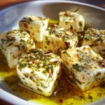 Close-up of cubes of marinated cheese soaking in olive oil with visible herbs and spices.