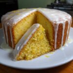 A slice cut from a moist lemon cake recipe, topped with a thick white glaze and lemon zest.