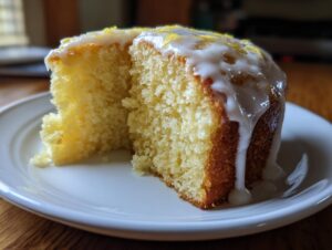 Close-up of a moist slice of lemon cake recipe with thick white glaze and lemon zest.