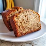 Close-up of two thick slices of moist vegan banana bread on a white plate.