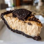 A thick slice of no bake peanut butter pie with a dark chocolate crust and a cookie garnish.