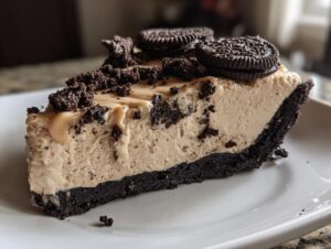 A decadent slice of no bake peanut butter pie featuring a dark chocolate crust and creamy filling, topped with Oreos.