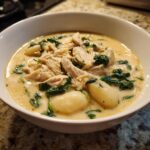 A close-up of a bowl of creamy Olive Garden Chicken Gnocchi Soup, featuring shredded chicken, plump gnocchi, and wilted spinach.