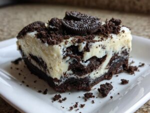 A rich, layered slice of Oreo fudge showing a dark chocolate base and creamy white filling, topped with cookie crumbs.