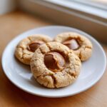 Three freshly baked peanut butter cup cookies with melted chocolate centers resting on a small white plate.