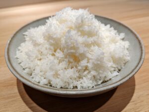 Close-up of fluffy, glossy, perfectly cooked sushi rice piled high in a rustic grey ceramic bowl.
