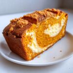 A close-up of a sliced loaf of vibrant orange pumpkin cream cheese bread with a visible cream cheese swirl and streusel topping.