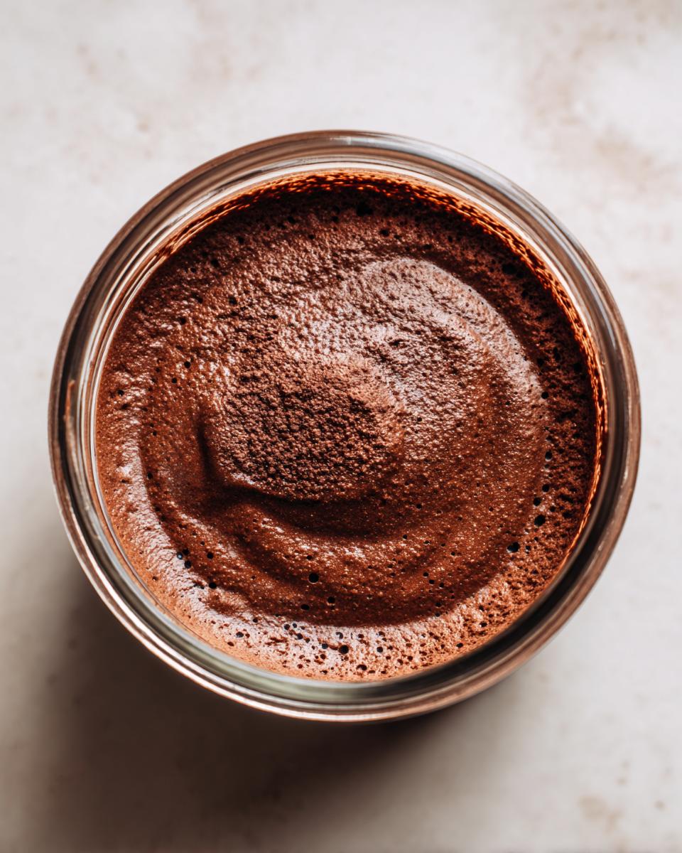 Overhead view of rich, airy chocolate mousse filling a small glass jar, showing textured peaks.