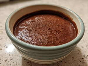 Close-up of rich, dark chocolate pudding topped with cocoa powder in a small, striped bowl.