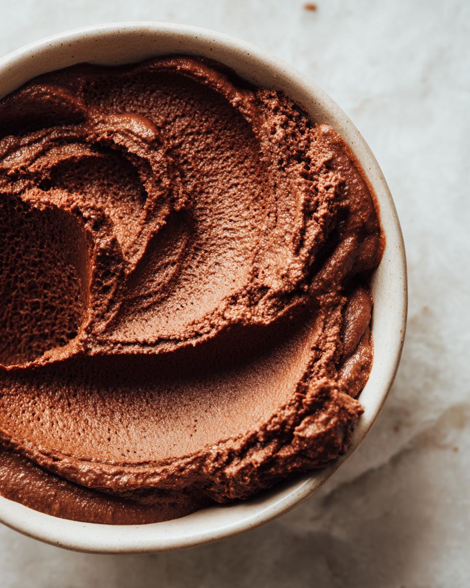 Overhead close-up of rich, dark chocolate pudding swirled beautifully inside a small, light-colored bowl.