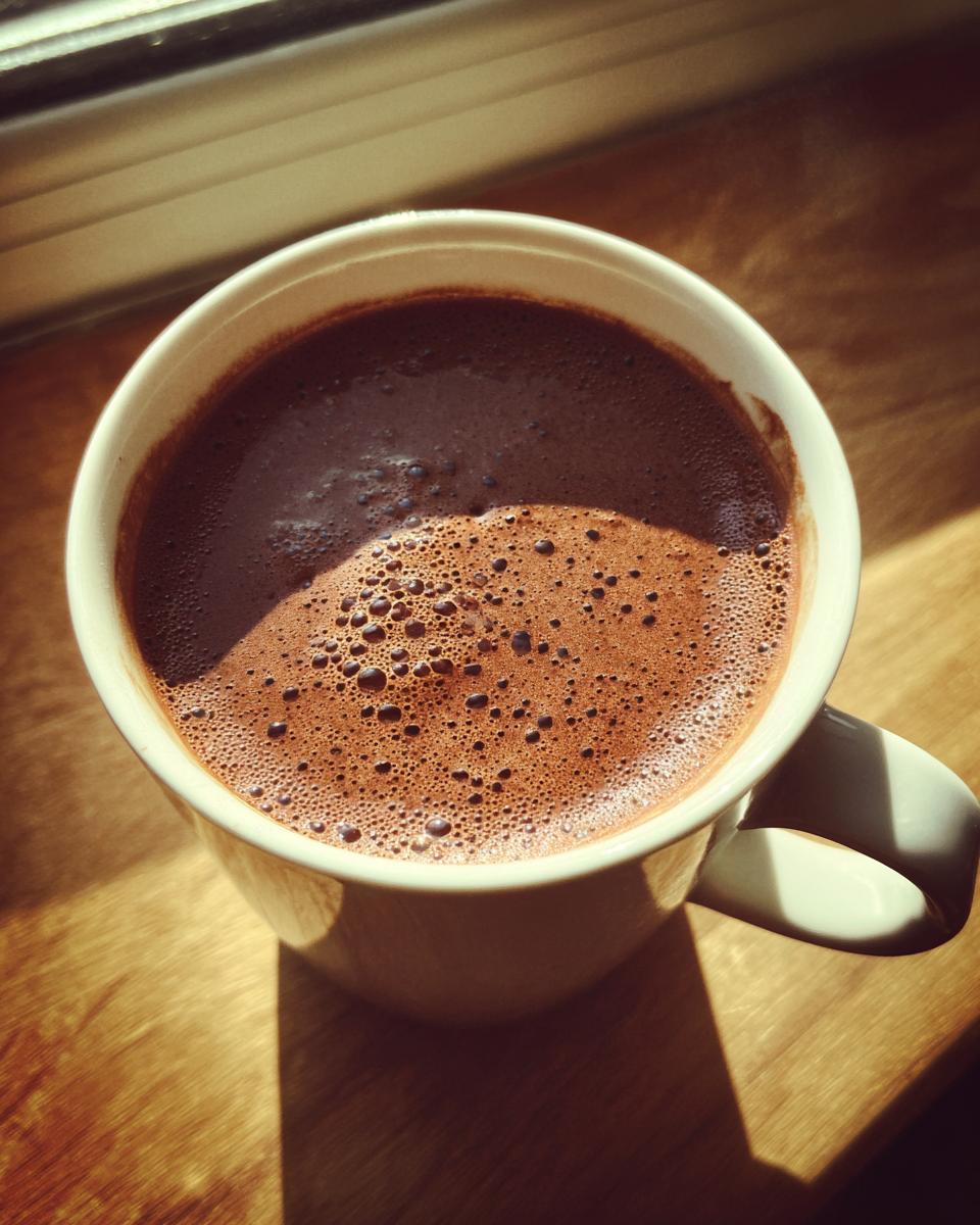 Top-down view of a rich, frothy french hot chocolate served in a white mug by a sunny window.