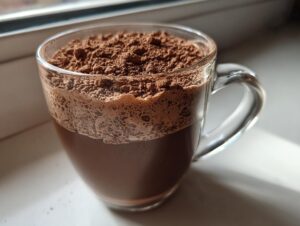 Close-up of a glass mug filled with rich hot cocoa mix, topped with a thick layer of cocoa powder.