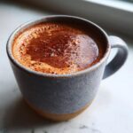 Close-up of a rich mexican hot chocolate with frothy top, served in a speckled blue and brown mug.