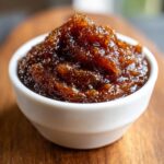 Close-up of thick, dark brown pear butter piled high in a small white bowl.