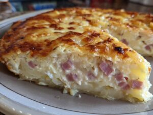 A close-up of a slice of baked scalloped potatoes and ham casserole with a golden, cheesy crust.